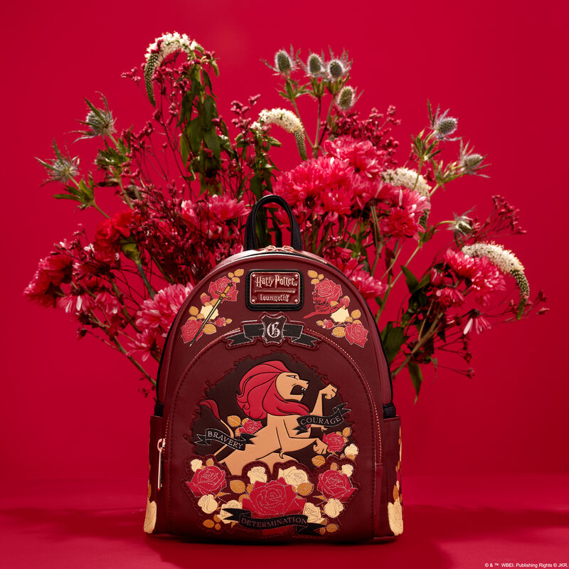 Red mini backpack featuring the Gryffindor lion on the front, surrounded by floral designs of white and red flowers, sitting against a red background in front of a real bouquet of white and red flowers 